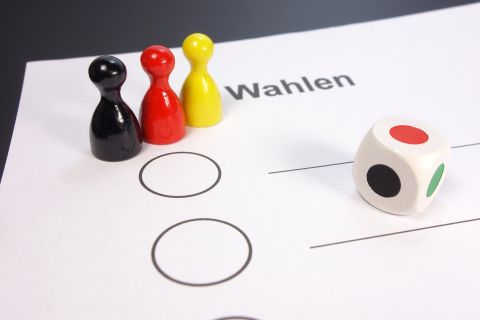 Spielsteine und Würfel auf einer Wahlkarte als Symbol für die ‚Qual der Wahl‘ in Graz.“
